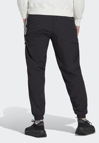 Mustat urheiluhousut, joissa on joustava vyötärö, kapeat lahkeensuut ja valkoiset somisteviivat sivuilla, valmistettu kevyestä, sileästä kankaasta.