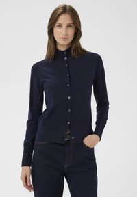 Tengerészkék kardigán könnyű köt�ött anyagból, magas nyakkal, gombsorral és bordás szegéllyel. Egyszínű, mintamentes kivitel.