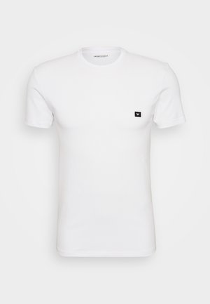 Balta trumpa rankovėmis marškinėliai, pagaminti iš minkštos medvilnės, su maža juoda logotipo etikete kairėje krūtinės pusėje. Klasikinis apvalus iškirpimas.