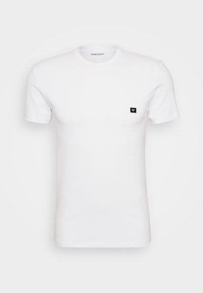 Balta trumpa rankovėmis marškinėliai, pagaminti iš minkštos medvilnės, su maža juoda logotipo etikete kairėje krūtinės pusėje. Klasikinis apvalus iškirpimas.