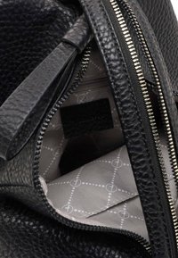 Zwarte leren handtas met een gestructureerde buitenkant, zilveren rits en een grijs gevoerd interieur met een geometrisch patroon. Inclusief een label binnenin.