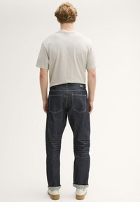 Camiseta gris ajustada, pantalones vaqueros de mezclilla azul oscuro con puños enrollados, diseño de cinco bolsillos, costuras claras, combinados con zapatillas blancas.