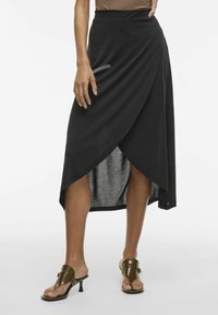 Black wrap skirt with a smooth texture, high-low hem, and a slightly draped front. Paired with brown open-toe heeled sandals.