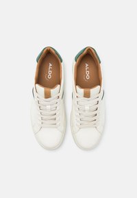 Sneaker bianco con accentuazione verde sul tallone, linguetta beige e striscia laterale nera. Presenta lacci testurizzati e una superficie liscia. Logo sulla soletta.