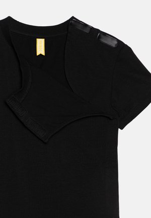Svart kortärmad T-shirt med rund hals. Flera svarta tryckknappar nära axeln och en gul varumärkesetikett inuti. Mjuk tyg.