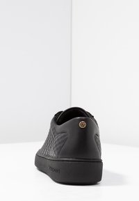 Sneaker in pelle nera con design trapuntato testurizzato, punta tonda e suola nera spessa. Presenta un accento del logo dorato sul tallone.