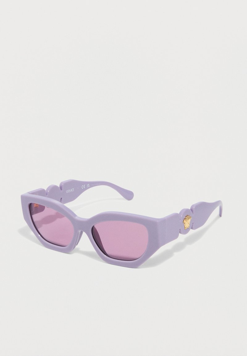 Μώβ γυαλιά ηλίου με σχήμα cat-eye, ροζ φακούς και χρυσό έμβλημα Medusa στο πλάι, παρουσιασμένα σε λευκό φόντο.