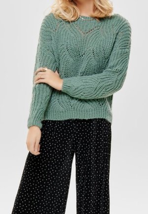 Maglione verde menta lavorato a maglia con motivo a rilievo, abbinato a pantaloni in velluto nero con pois bianchi. Vestibilità comoda; maniche lunghe.