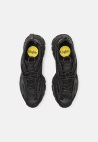 Chaussures de sport noires avec une tige texturée, des panneaux en maille et une semelle en caoutchouc proéminente. Détails du logo jaune sur la semelle intérieure.