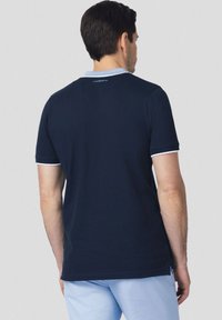 Granatowa koszulka polo wykonana z bawełny, z jasnoniebieskim kołnierzykiem z białym wykończeniem i logo na plecach. Krótkie rękawy i klasyczny krój.