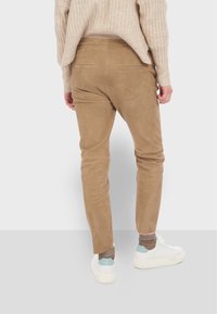 Tan slim-fit byxor gjorda av mjukt material, med en slät textur och två bakfickor. Kombineras med vita sneakers och strumpor.