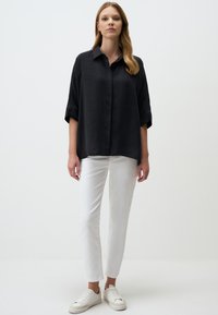 Black button-up shirt with rolled sleeves, paired with white slim-fit pants and white sneakers. The fabric has a smooth, subtle sheen.