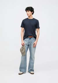 Navy kokvilnas T-krekls, gaiši zili plaša griezuma džinsi, brūns josta, tur pelēku cepuri. Ikdienišķs apģērbs ar vienkāršām, tīrām līnijām un nomierinošām krāsām.