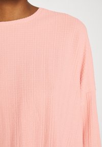 Vaaleanpunainen tekstuuri paita, jossa on pyöreä kaula-aukko, ribattua kuviota ja löysät hihat rentoa siluettia varten.