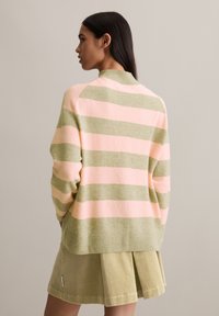 Gestreifter Pullover in pinken und grünen Farbtönen, weiche Textur und gerippter Ausschnitt. Kombiniert mit einem passenden Cordrock.