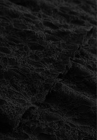 Čierna čipková látka s prepracovanými kvetinovými vzormi a textúrovaným povrchom, s jemnými skladmi a delikátnymi okrajmi.