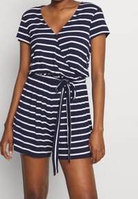 Námořnický modrý overal s bílými pruhy, krátkými rukávy, véčkovým výstřihem a stahovací šňůrkou v pase. Měkká, pružná látka s uvolněným střihem.