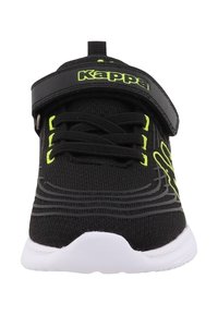 Fekete sportcipő légáteresztő szövet felsőrésszel, neon zöld részletekkel, állítható pánttal és fehér gumi talppal, amelyen texturált rések találhatók.
