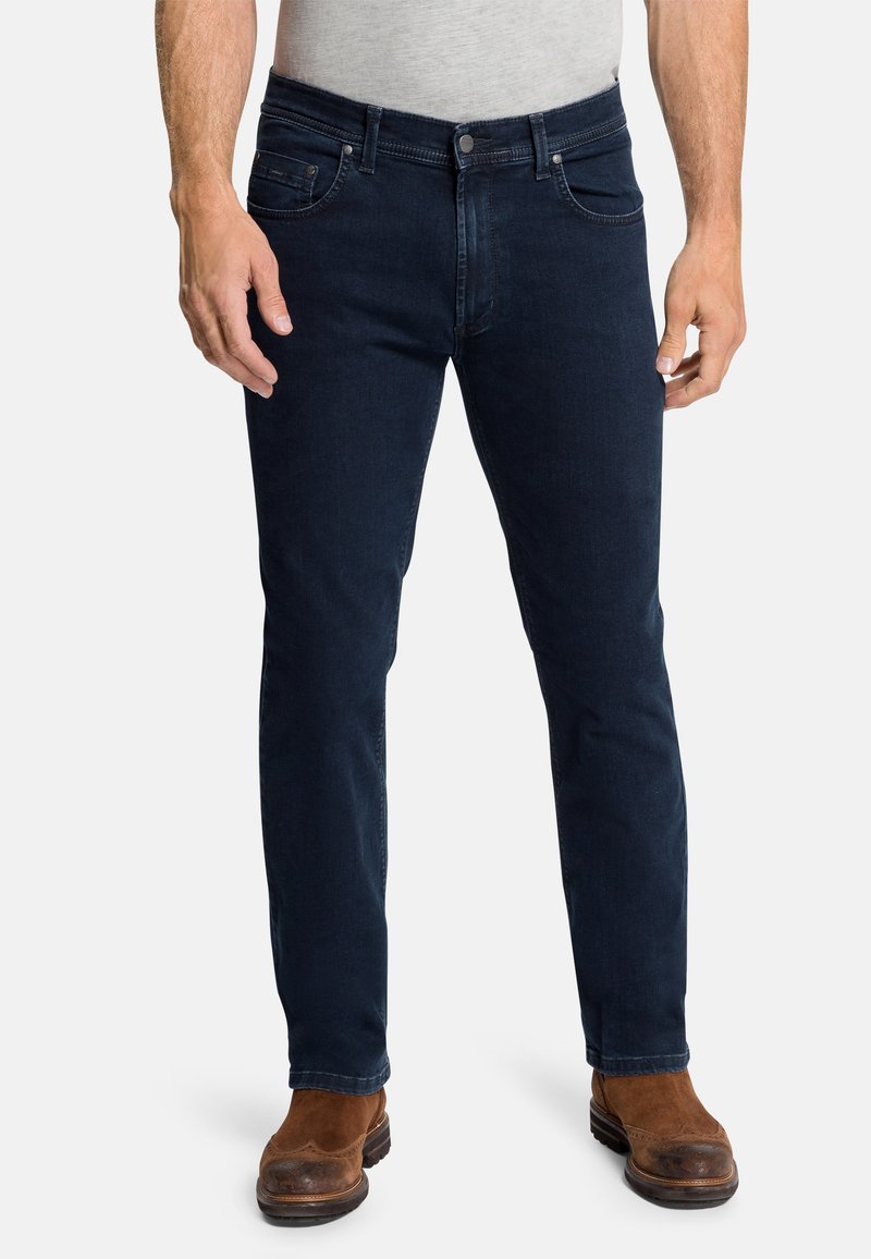 Dunkelblaue Denim-Jeans im Slim Fit, mit fünf Taschen, einem Reißverschluss und einer dezenten, verblassten Textur. Kombination mit braunen Lederstiefeln.