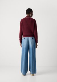 Maglione bordeaux a coste con colletto, abbinato a jeans in denim azzurro chiaro a gamba larga, entrambi caratterizzati da un design semplice e senza motivi visibili.