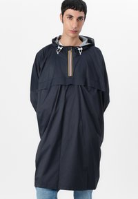 Marineblå, lett, vanntett poncho med hette, halv-glidelås foran og stripete detaljer. Har en løs passform og glatt tekstur.