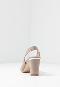 Taupe mockasinfärgade blockklackssandaler med slingbackrem och en tunn guldaccent nära toppen av klacken.