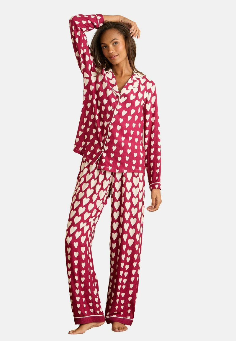 Ensemble de pyjama à motifs cœurs rouge et blanc, comprenant un haut à boutons et un pantalon à taille élastique, fabriqué dans un tissu doux et offrant une coupe décontractée.