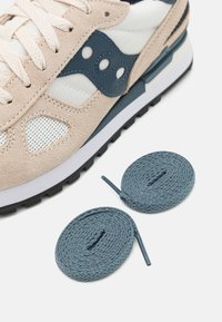 Saucony sneaker bézs színű velúrbőr és hálós felsőrésszel, navy kiegészítőkkel, fehér panelezéssel és sötét talppal, kék fűzőkkel kiegészítve.