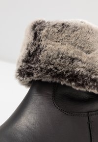 Črne usnjene gležnjače z mehkimi sivo krznenimi robovi. Gladka struktura z vidnimi šivi in mehak umetni krzneni podložek.