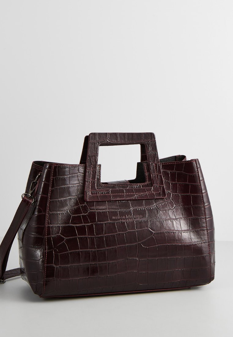 Borsa in finta pelle coccodrillo bordeaux con manico a taglio quadrato, forma strutturata e tracolla rimovibile. Texture liscia, design minimalista.