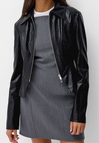 Czarna skórzana kurtka o dopasowanym kroju, srebrny zamek błyskawiczny, stożkowy kołnierz i długie rękawy, zestawiona z szaro-sukienką.