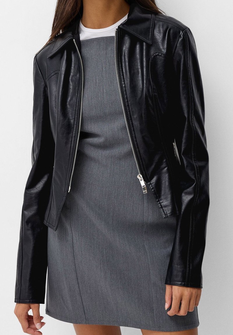 Czarna skórzana kurtka o dopasowanym kroju, srebrny zamek błyskawiczny, stożkowy kołnierz i długie rękawy, zestawiona z szaro-sukienką.