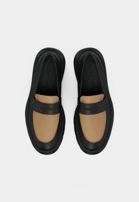 Černé a hnědé nazouvací boty s hladkým koženým svrškem, kontrastními barevnými panely a raženým logem na pásku. Zaoblená špička.