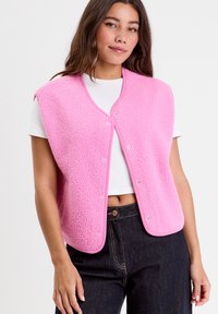 Fleece pink vest with a rounded neckline and snap buttons, featuring a textured surface and contrasting trim. Worn over a white shirt.