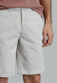 Lichtgrijze shorts van katoen. Tot de knie met een rechte snit, voorzien van een voorke pocket en een omgeslagen zoom. Minimaal zichtbaar stiksel detail.
