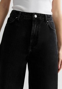 High-waisted black denim jeans with a slightly faded finish, featuring a front button closure, belt loops, and side pockets.