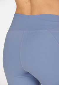 High-waisted blue leggings made of smooth, stretchy material with flat seams and a subtle logo at the waistband.