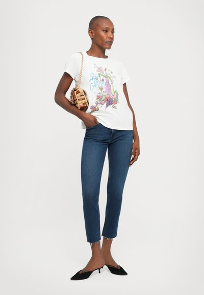 Witte graphic t-shirt met kleurrijk ontwerp, blauwe jeans, zwarte puntige instapschoenen en een kleine handtas met patroon.