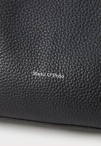 Borsa in pelle nera con una texture a granuli. Il nome del marchio "Marc O'Polo" è impresso in argento sul davanti.