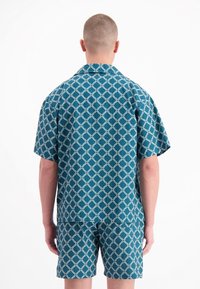 Korte mouw teal shirt en bijpassende shorts met een wit geometrisch patroon. De stof lijkt licht en heeft een ontspannen pasvorm.