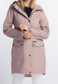 Veste imperméable rose avec capuche, fermetures à boutons et pressions, deux grandes poches avant, et un logo discret sur la poitrine. Texture lisse.