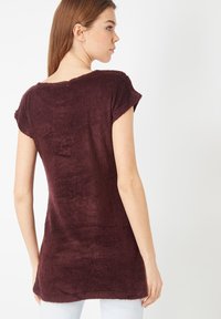 Túnica burdeos texturizada con mangas cortas y escote redondeado, que cae suavemente por debajo de las caderas con un acabado suave y aterciopelado.