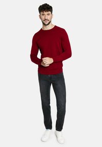 Suéter rojo de manga larga hecho de tejido suave, combinado con jeans oscuros y zapatillas blancas. El suéter tiene un escote redondo y mangas ajustadas.