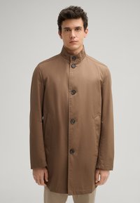 Bruine, lichte jas met een hoge kraag, sluiting met knopen aan de voorkant, twee zijzakken en een gladde textuur. Eenvoudig ontwerp en rechte snit.