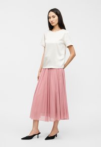 Λευκό σατέν τοπ με κοντά μανίκια σε συνδυασμό με ροζ πλισέ φαρδιά φούστα, ολοκληρωμένο με μαύρα παπούτσια μυτερά.