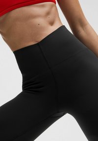 Leggings neri a vita alta realizzati in un tessuto liscio e elasticizzato, con cuciture piatte, progettati per offrire comfort e una silhouette aderente.