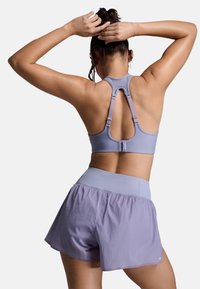Fialová športová podprsenka s textúrovanou tkaninou a nastaviteľnými ramienkami, doplnená o voľné, ľahké fialové šortky s vysokým pásom.