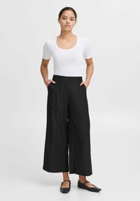 Svarta vida byxor med platt midja och sidfickor, tillsammans med en åtsittande vit t-shirt med kort ärm och svarta platta skor.
