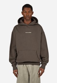 Καφέ φούτερ με μπροστινή τσέπη, κουκούλα με κορδόνια και λογότυπο "PEGADOR" σε λευκό στο στήθος, σε απλό λευκό φόντο.