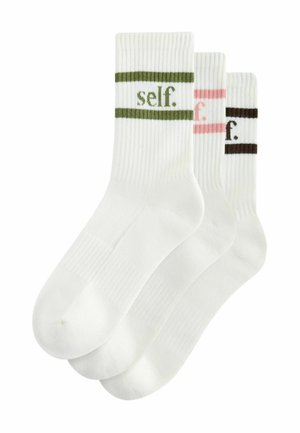 Drei Paar weiße Socken mit geripptem Muster. Jede Socke hat einen farbigen Streifen – grün, rosa und braun – und das Wort "self." in Kleinbuchstaben.